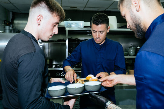 Professional chefs preparing plates arranging appetizers in kitchen