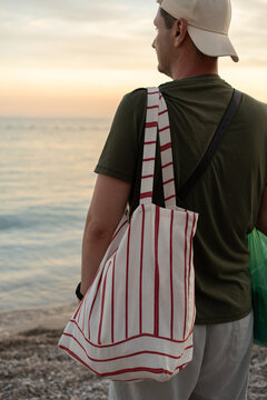A man carrying a striped tote bag at the shoreline