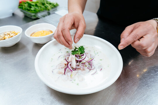 Chef garnishing peruvian ceviche with fresh cilantro in kitchen