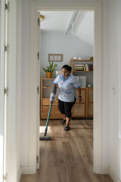 Housekeeper vacuuming floor performing domestic cleaning service