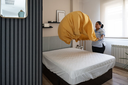 Housekeeper tidying bed, changing bedsheets in bedroom