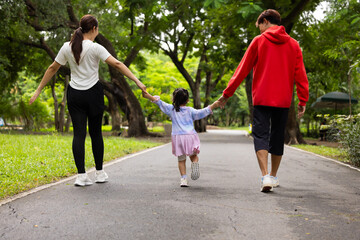 Obraz premium Backview Parents reate perfect day for childrent. Father and mother hands and raise her up and walk. exercising and walking together in city park summer. healthy lifestyle in nature. family bonding