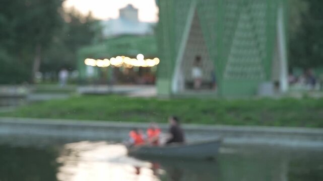 Blurry bokeh background of people rowing boat in park pond.
