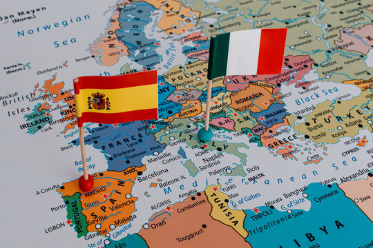 Close-up of a map with Spanish and Italian flag pins, highlighting Schengen border controls, diplomatic tension, and European migration crisis.