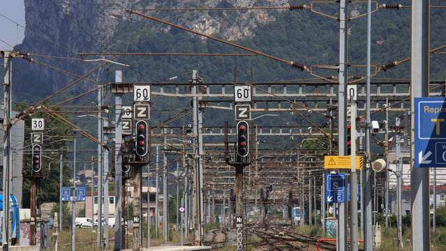 Gare de montagne avec des voies ferr&eacute;es et des syst&egrave;mes &eacute;lectriques a&eacute;riens panneaux indiquant une vitesse maximale de 60 km/h, signaux lumineux rouges, infrastructures de signalisation ferroviaire.