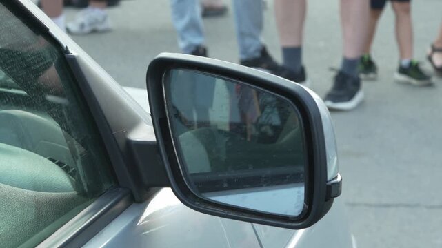 Close-up of a silver car side wing mirror on street.