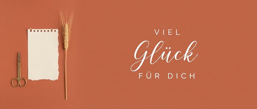 Good luck German greeting card flatlay with notepad, wheat, and scissors on terracotta background featuring Viel Gl&uuml;ck F&uuml;r Dich text for rustic congratulation banner design background layout.