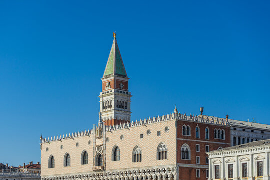Doge's Palace facade and St Mark's Campanile bell tower under clear blue sky in Venice, Italy.