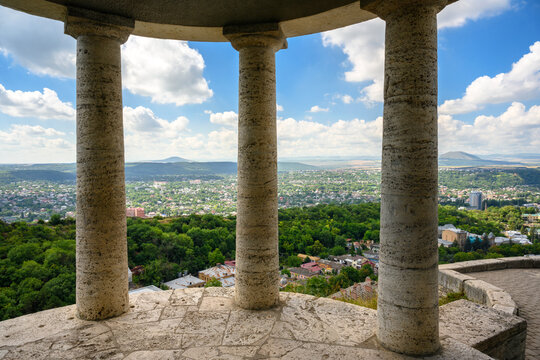 View of a city and distant mountains framed by stone columns of a classical rotunda, Pyatigorsk, Russia. Elevated observation deck overlooking a green valley on summer day