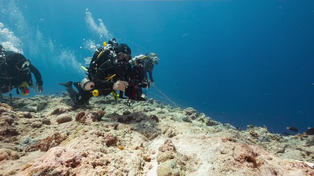 Underwater shot of male SCUBA Diver with underwater camera hooked onto the reef in strong current in the Palau Marine Sanctuary