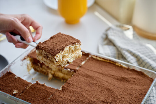 Serving tiramisu slice from a glass dish, lifted with a spatula after cutting