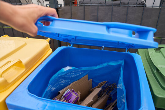 Hand opens blue recycling bin containing flattened cardboard for paper recycling