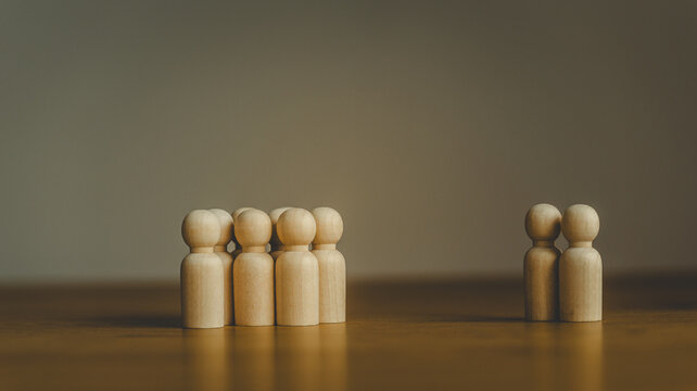 Wooden peg figures representing a group separated from a couple on a wooden surface