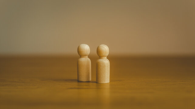 Two wooden peg dolls standing side by side on a wooden surface