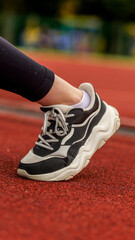 Fototapeta premium Close-up of a person wearing a black and white athletic shoe on a red track
