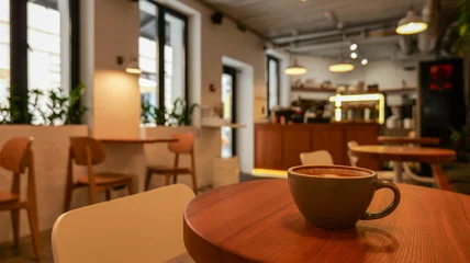 Fototapete Gastronomie Cozy coffee shop interior with a warm cup of coffee on a wooden table  © shine.graphics