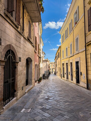 Fototapeta premium Scenic View of a narrow pared alley in an ancient Italian Village City, featuring colorful historic buildings with wooden shutter, vintage street lamps and a Church dome visible in the background agai