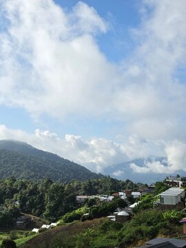Beautiful green mountain ridge under bright blue sky and white clouds with a small rural village at the foothills.