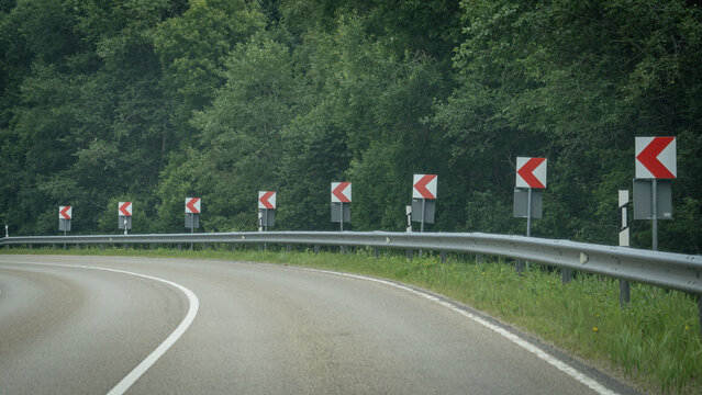 Empty curved forest road lined with chevron signs and guardrail