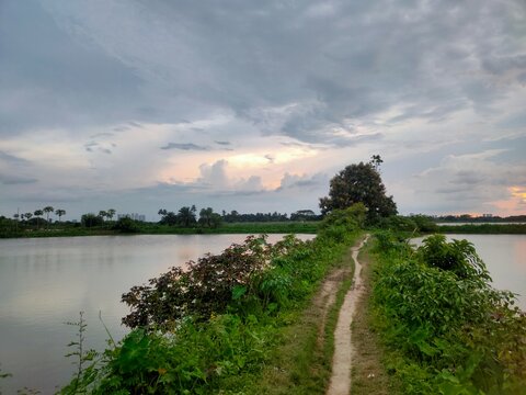 Narrow soil path in between water bodies, village landscape view 