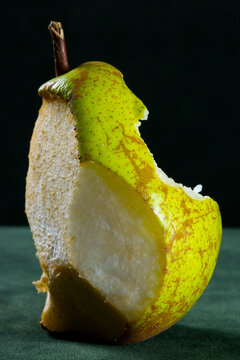 Ripe pear, bitten and trimmed, against a dark background.