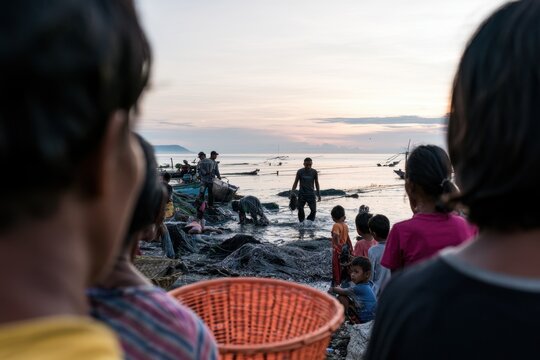 children watch as a fisherman works on the shore at dawn in indonesia