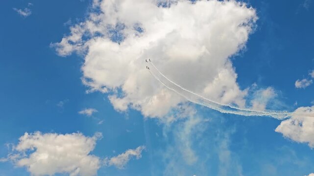 Aerobatic stunt aircrafts performing spectacular aerial maneuvers in the sky, releasing colorful smoke and fireworks. Team formation flight with white smoke trails. 4K video footage