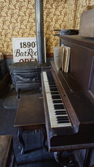 Antique upright piano and cast iron wood stove inside a preserved nineteenth-century Victorian interior with decorative wallpaper and ceiling. © lensbyMehlika