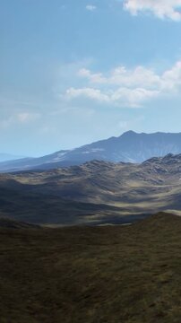 A wide view of mountains and valleys shows natures landscape. The scene features hills with varying heights under a blue sky filled with clouds during the day.