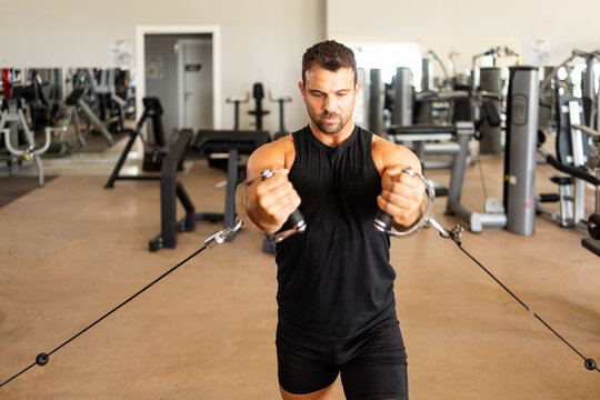 A man in his 40s performing a standing pulley chest fly exercise in a modern gym, developing upper body strength, chest muscles and functional fitness with resistance training.