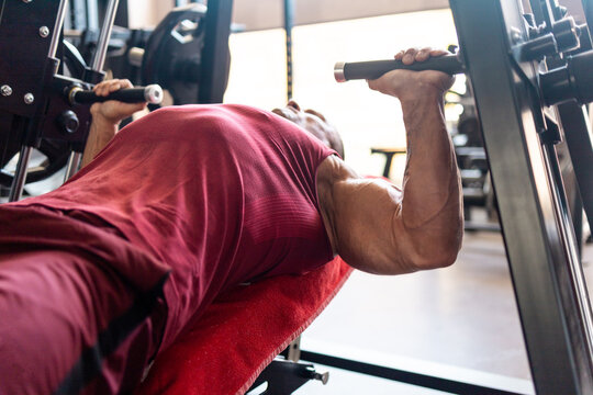 Muscular man performing chest press on a strength training machine in a modern gym, close-up of upper body during intense weightlifting workout.