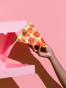 Hand hold pepperoni pizza slice beside open pink box