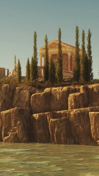 A structure sits atop a rocky cliff overlooking water. Tall trees grow nearby. The sky is clear and the sunlight brightens the scene. This place shows a mix of nature and ancient design.
