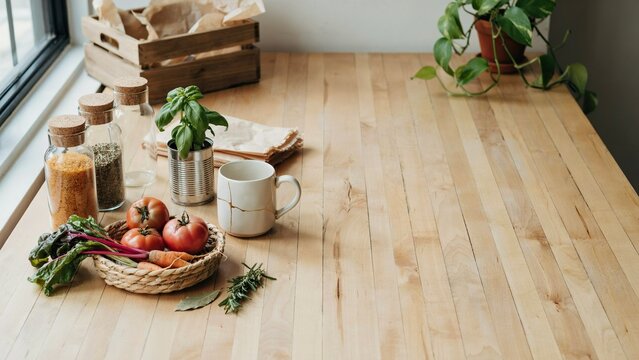 Vegetables and cooking ingredients sit neatly organized on a clean wooden kitchen countertop near a bright window.