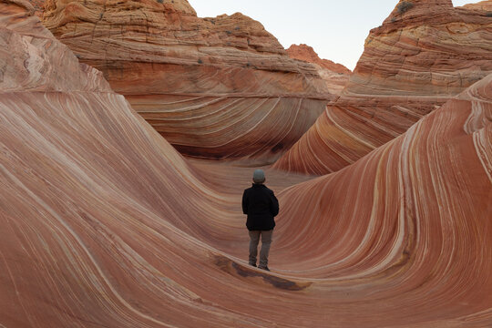 A woman wearing a coat and hat stands looking out at The Wave formation in Coyote Buttes North in the Paria Canyon Vermillion Cliffs wilderness, in Southern Utah and Northern Arizona.