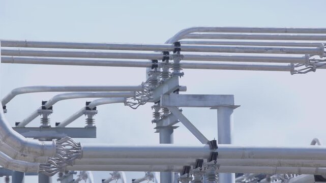 Industrial metal pipes and conduits spanning power substation rooftop with reflective silver surfaces, electricity equipment.
