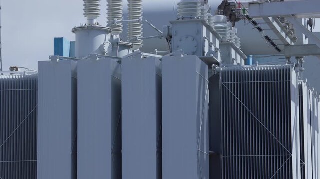 Electricity equipment high voltage transformer units at outdoor electrical substation facility during daytime.
