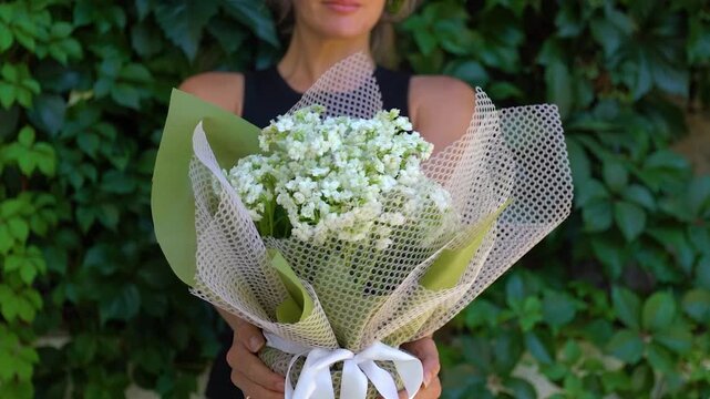 Unrecognizable woman holds a wrapped white gypsophila flower bouquet outdoors. Romantic floral gift represents anniversary celebrations, Mother's Day and florist services