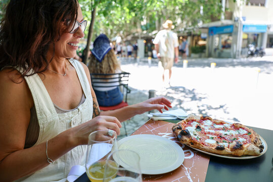 A woman enjoys a pizza at an outdoor caf&eacute; in Athens, Greece, surrounded by summer light and the relaxed atmosphere of Mediterranean street dining.