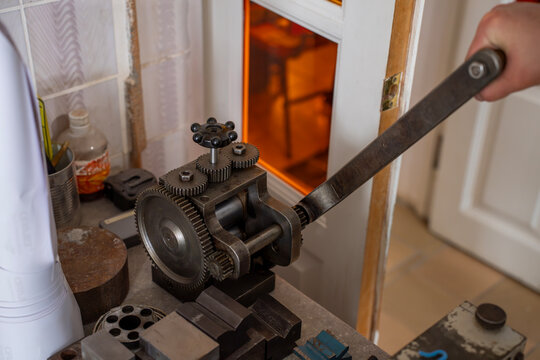 Hand rotating handle of manual rolling mill machine on workbench in jewelry workshop for flattening and shaping metal wire or sheet.