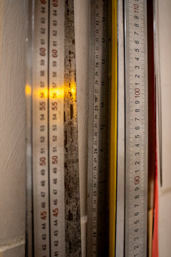 Metal measuring rulers with printed millimeter and centimeter scale markings hanging vertically on workshop wall for precision alignment.