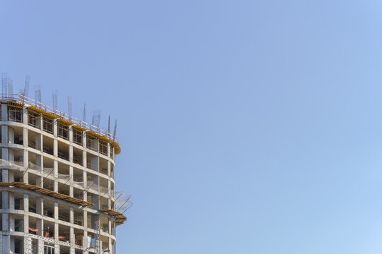 A monolithic concrete framework of a multi-story residential building under construction with reinforcement bars. A minimalist urban architecture background with plenty of copy space.