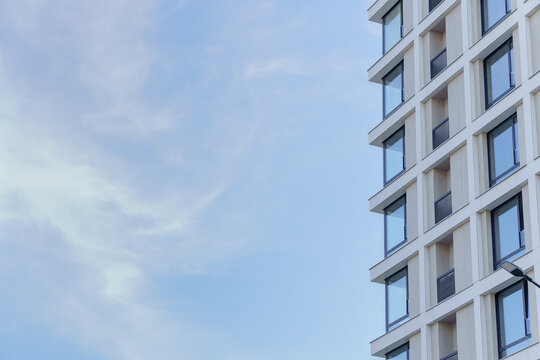 A modern residential building facade with geometric glass windows and a white concrete exterior. A contemporary urban apartment skyscraper corner with extensive sky copy space.