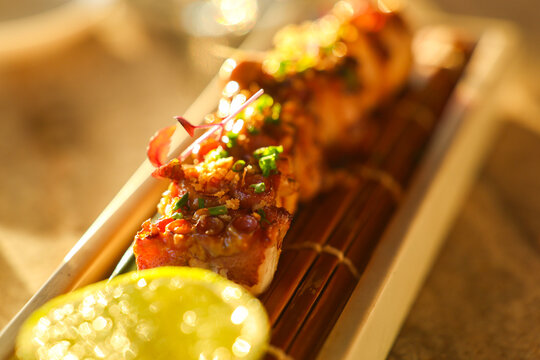 Grilled seafood skewer garnished with herbs and seasoning, served with a fresh lime wedge in warm evening light at a Mediterranean restaurant.