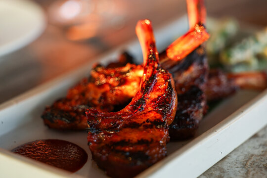 Glazed grilled lamb chops with rich char marks and dipping sauce served on a white plate, capturing the warmth and flavor of Mediterranean cuisine in Greece.