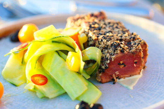 Seared tuna coated with sesame seeds and served with fresh cucumber ribbons and vegetables, showcasing elegant seafood cuisine and gourmet restaurant presentation.