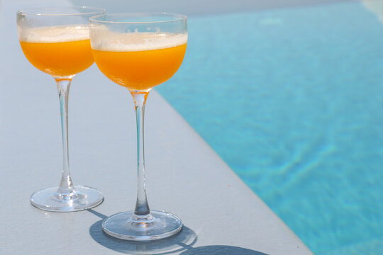 Two orange cocktails beside a swimming pool, capturing luxury travel, relaxation, and hospitality in a sunny outdoor setting.