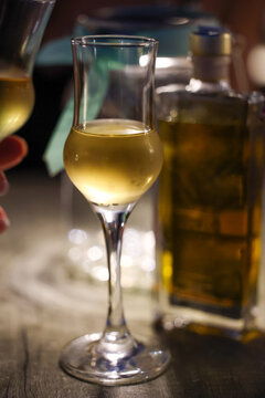 A slender glass of golden liqueur beside its bottle glows under warm evening light in Greece, evoking Mediterranean elegance and refined dining.
