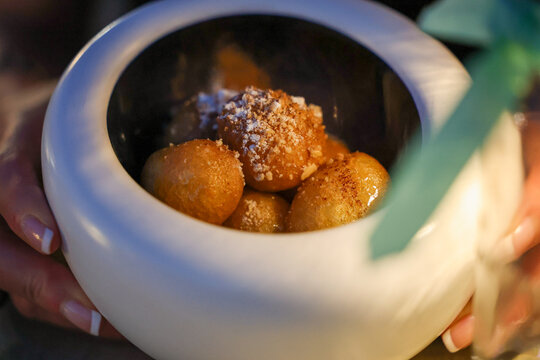 Golden fried dessert bites served in a ceramic bowl with a sweet glaze and crumb topping, presented as an elegant restaurant dessert.