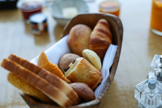 Assorted breakfast pastries and breads served in a basket, including croissants and rolls, presented as a fresh continental breakfast spread.